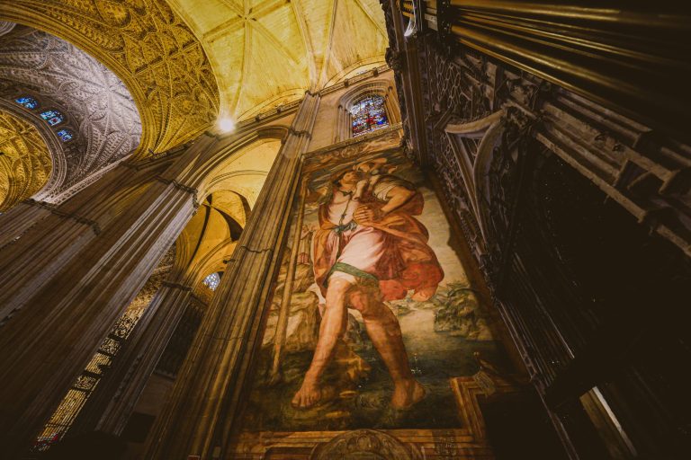 Ornate cathedral ceiling with large wall painting and stained glass window.
