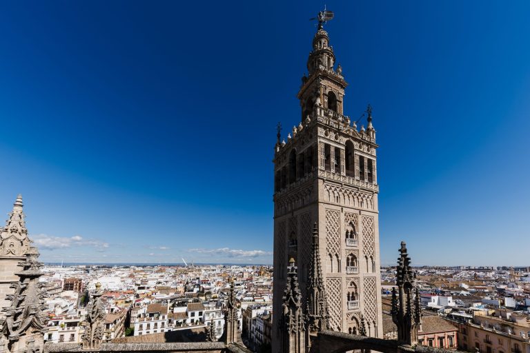 View of a tall, ornate tower against a clear blue sky with a cityscape in the background.