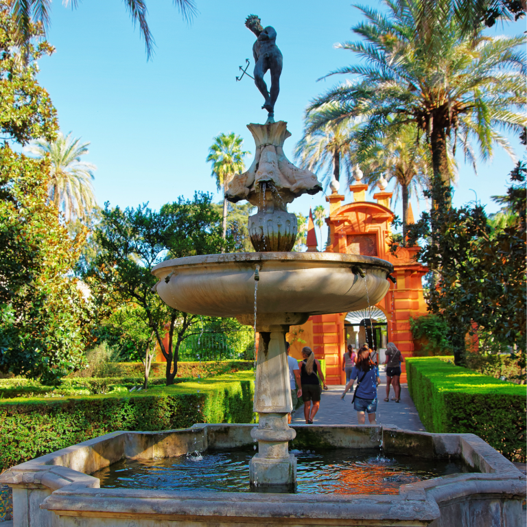 People walking by a decorative fountain in a lush garden.