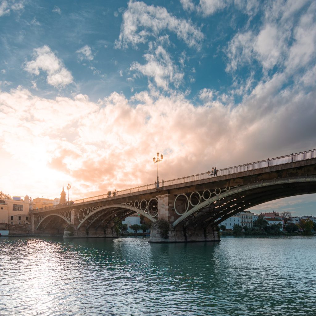 Bridge over a river with a dramatic cloudy sky at sunset.