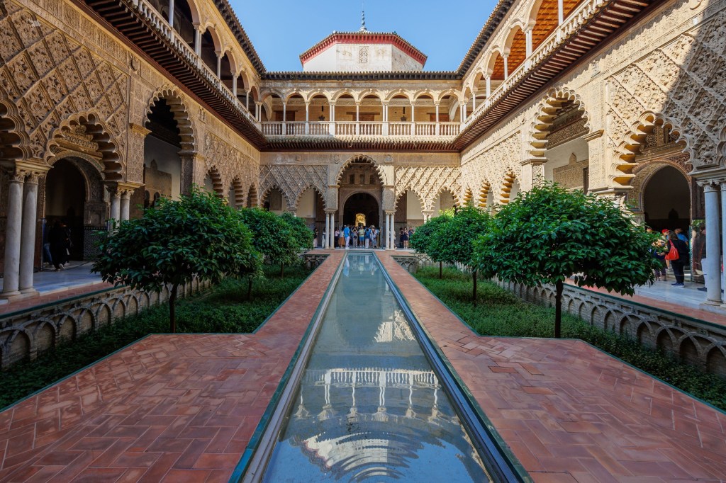 Ornate courtyard with arches, pond, and green shrubs in historic building.