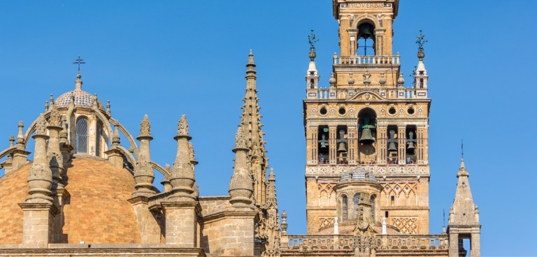 Historic cathedral with tall bell tower and spires under blue sky.