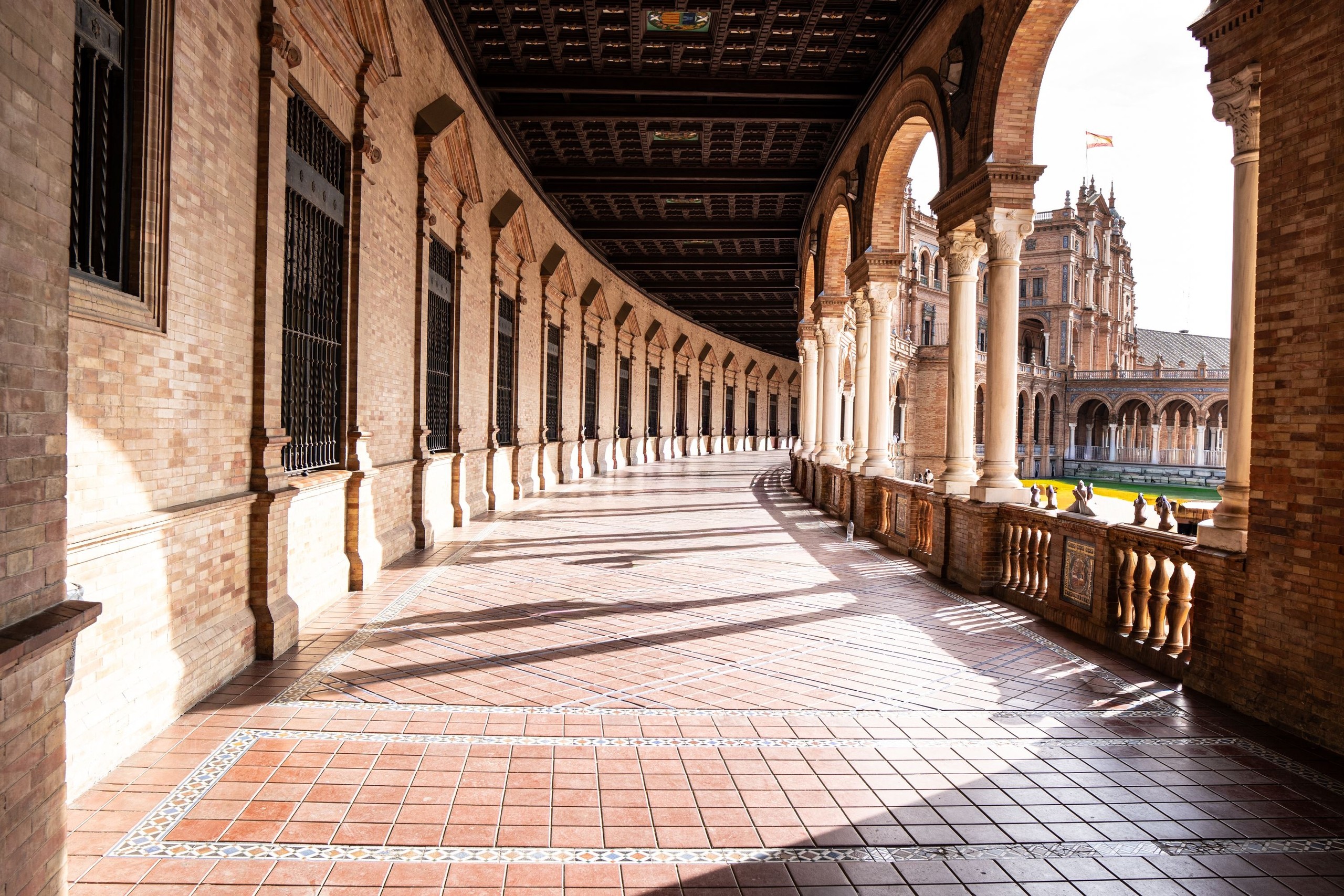 Curved corridor with arches and brick walls in sunny outdoor setting.