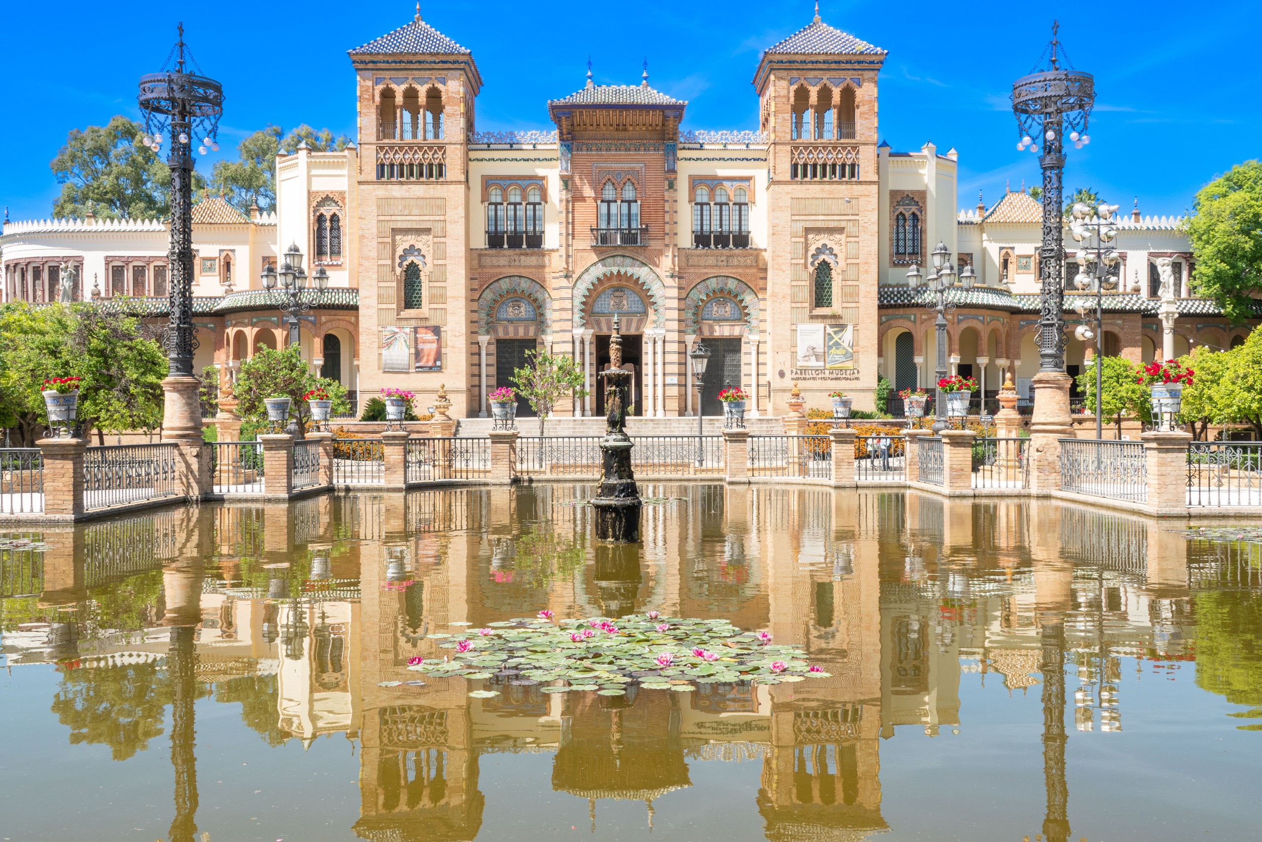 Historic building with towers reflected in a pond, clear blue sky.