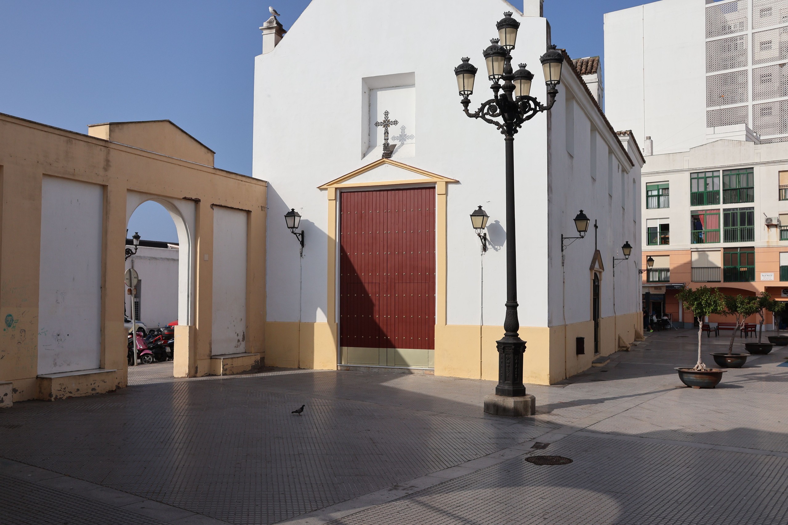 Small white church with red door and street lamps in a plaza.
