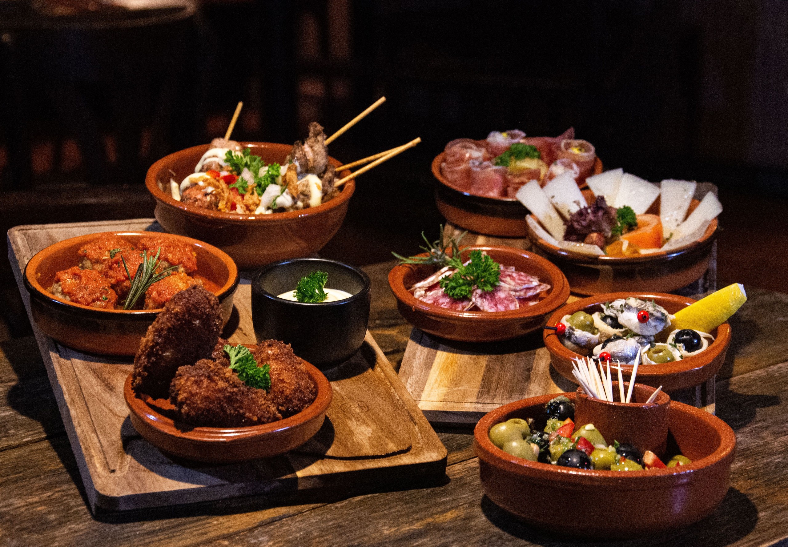 Assorted tapas dishes in clay bowls on wooden table.