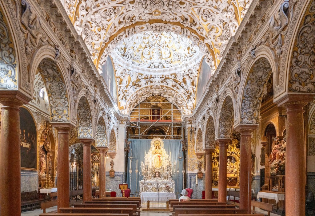 Ornate church interior with detailed arches and a statue at the altar.