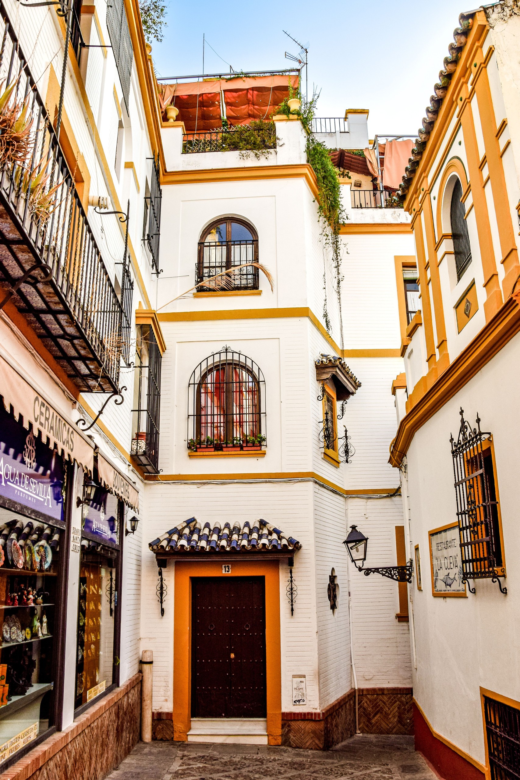 Narrow alley with white buildings, arched windows, and decorative ironwork.
