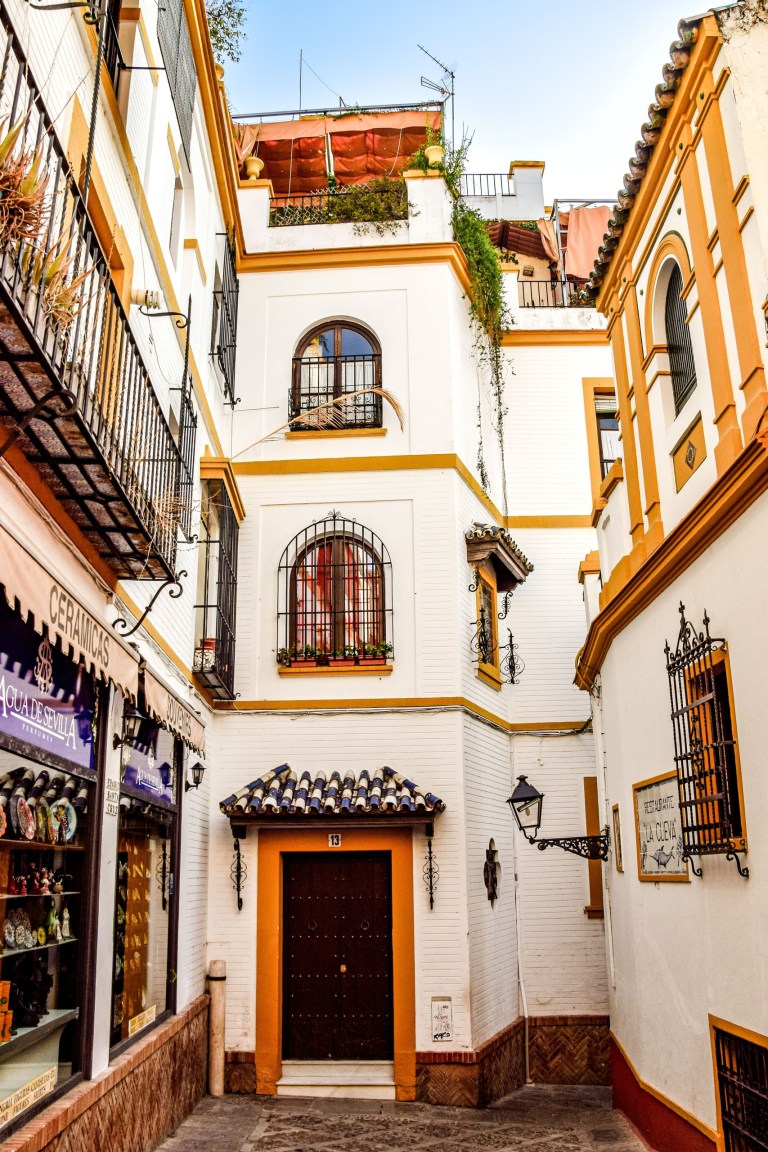 Narrow alley with white buildings, arched windows, and decorative ironwork.
